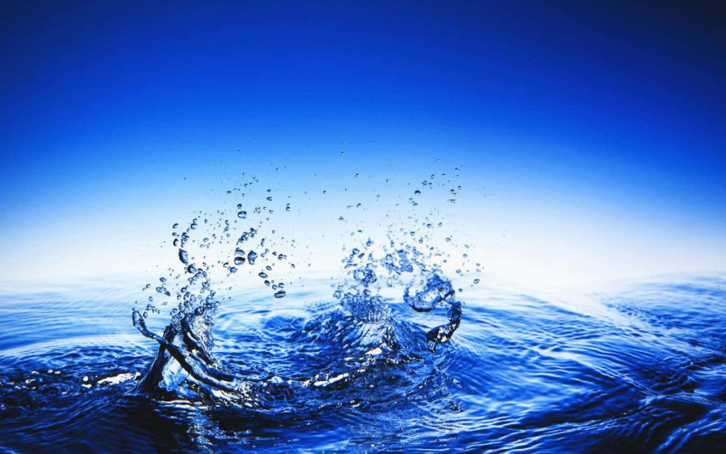 High-speed water splash with vibrant droplets on blue surface and bright gradient sky background Wallpaper