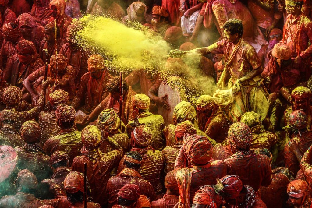 Holi festival in India vibrant crowd covered in red yellow gulal powder throwing colors celebration Wallpaper