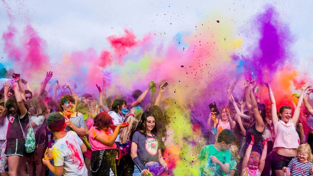 Vibrant Holi Festival crowd throws colorful powder creating rainbow clouds bright wallpaper background
