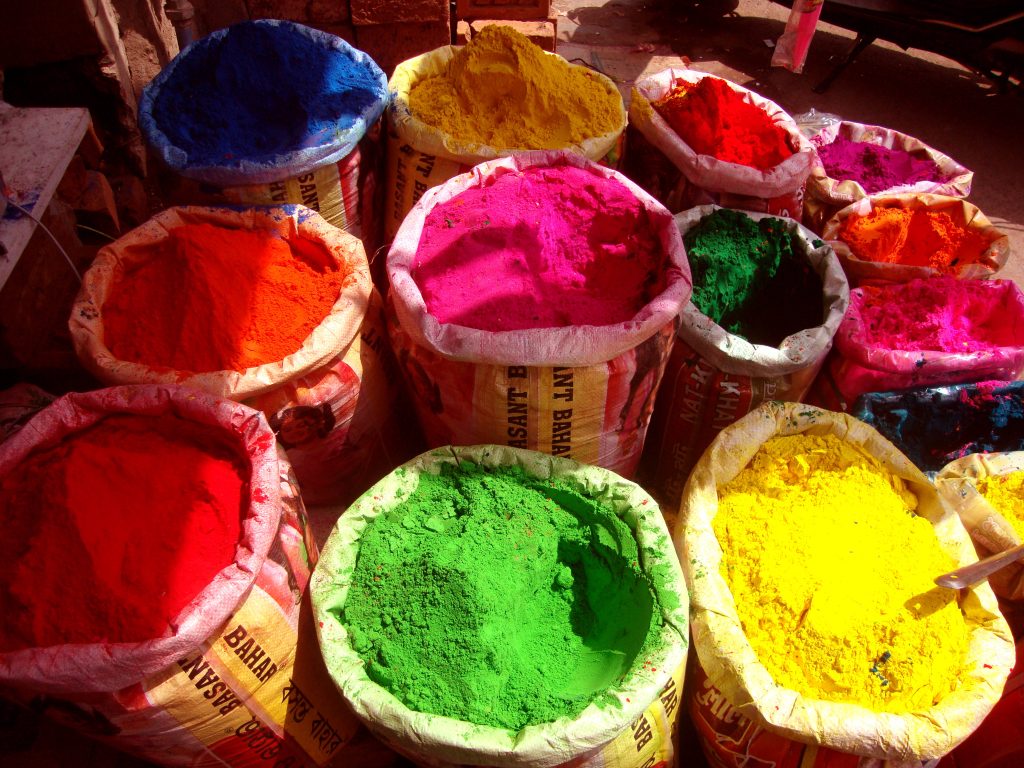Sacks of vibrant Holi powder pigments in red yellow green and pink at festive market background Wallpaper