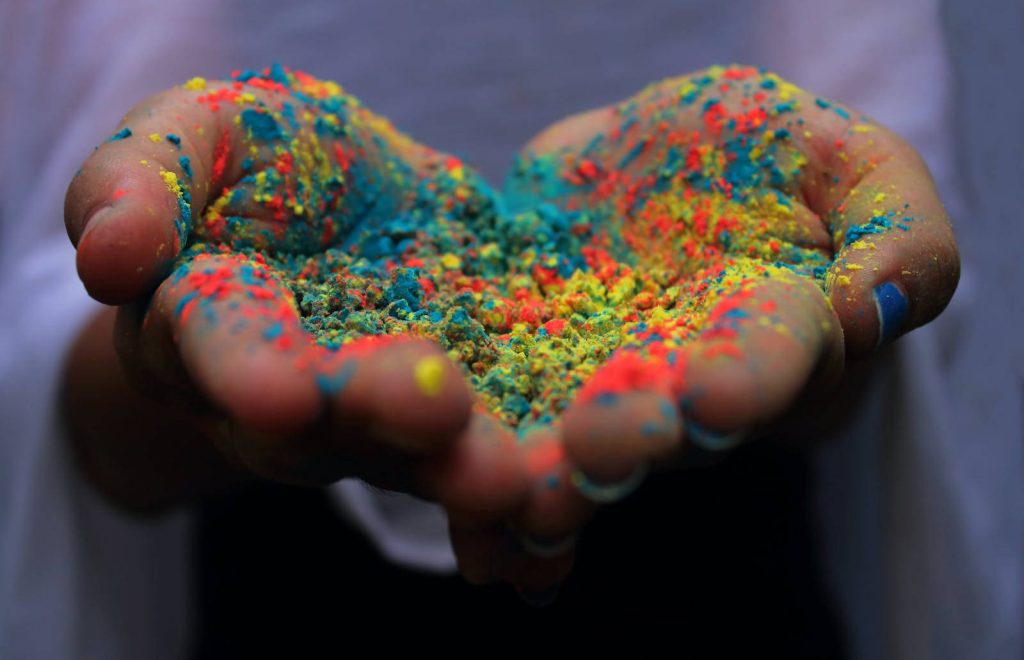 Cupped hands holding vibrant blue yellow and red Holi powder colorful festival of colours celebration Wallpaper
