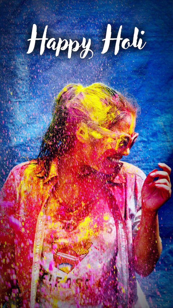 Smiling person covered in yellow and pink Holi powder on blue background celebrating festival Wallpaper