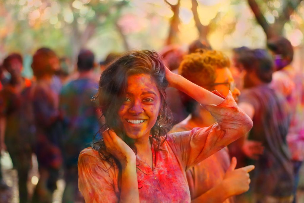 Smiling woman covered in Holi colors celebrates with joyful crowd in sunlit festive scene wallpaper