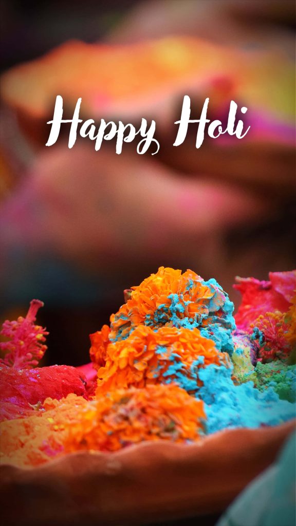 Macro of marigold flowers with blue orange pink gulal powder and Happy Holi text background Wallpaper