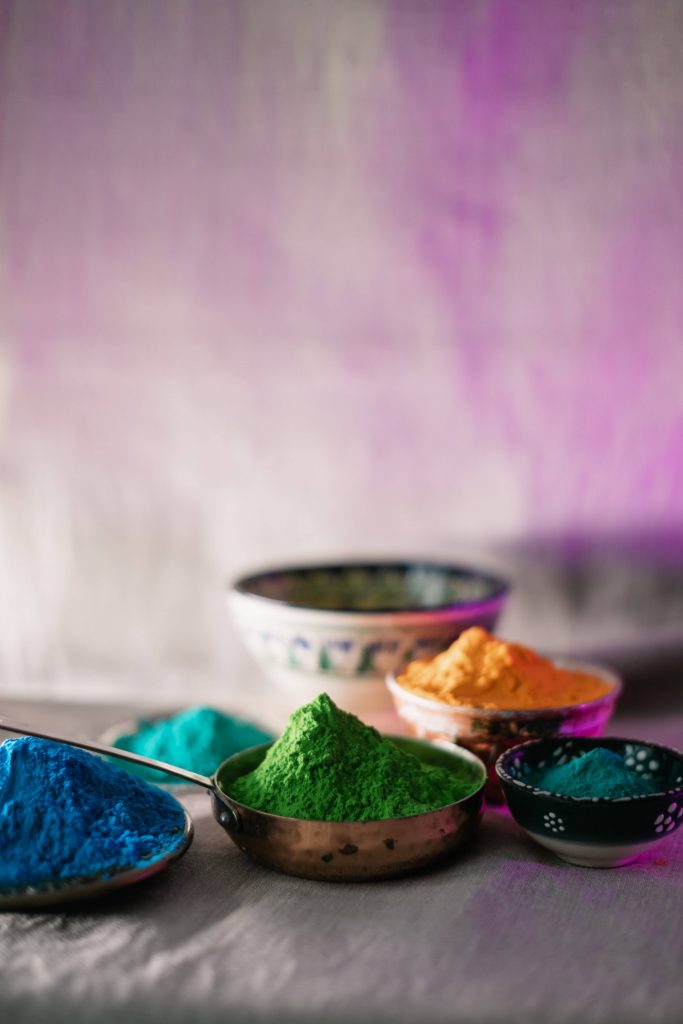 Vibrant Holi festival wallpaper with colorful Gulal powder in blue green and yellow bowls close-up