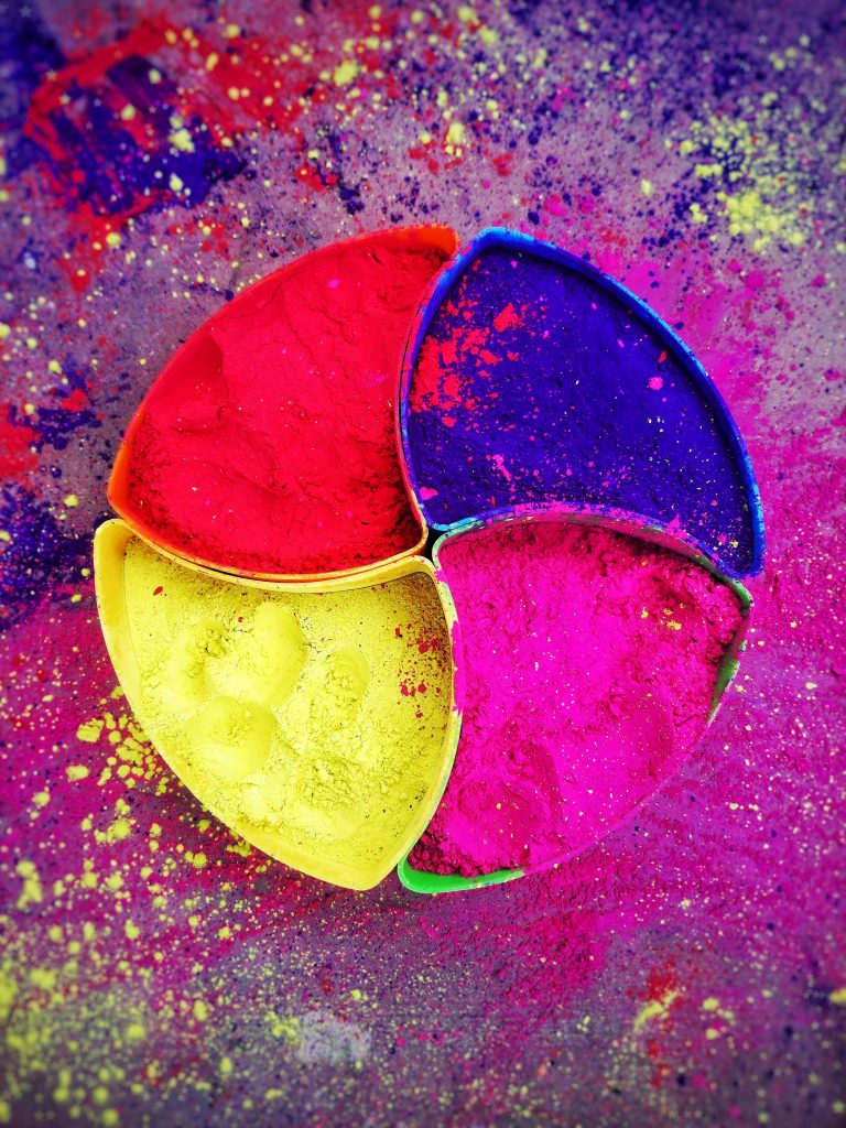 Top-down vibrant Holi wallpaper with segmented plate of bright red yellow blue and pink Gulal powder