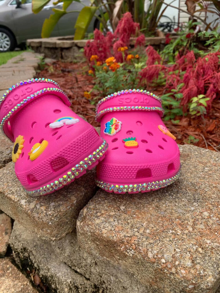 Hot pink Crocs with charms and rhinestones in a vibrant garden background wallpaper