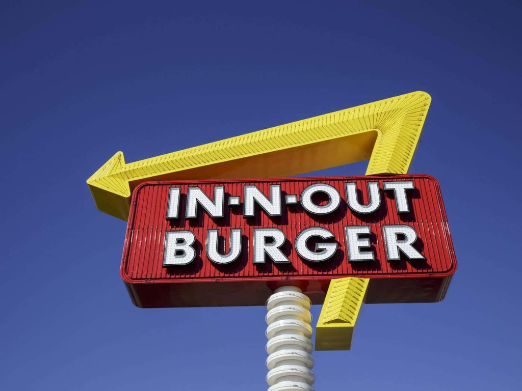 In-N-Out Burger red and white sign with yellow arrow against bright blue sky wallpaper background