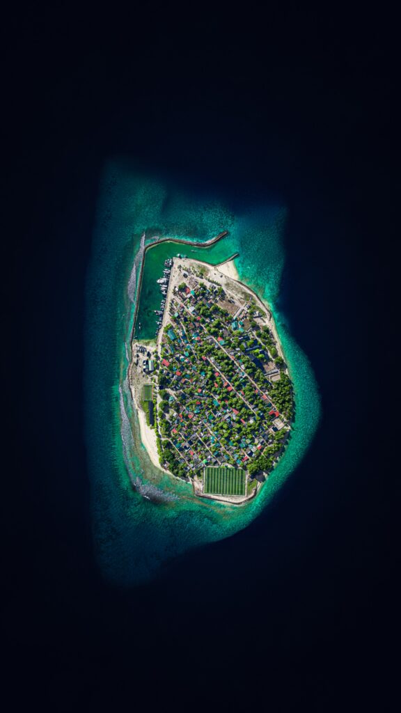 Top-down view of vibrant island with colorful buildings and lush greenery surrounded by blue sea Wallpaper
