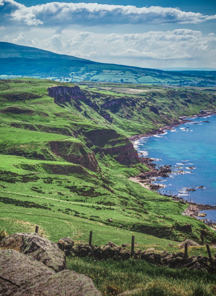 Vibrant island coastline wallpaper with green cliffs blue sea rolling hills and rocky shores view