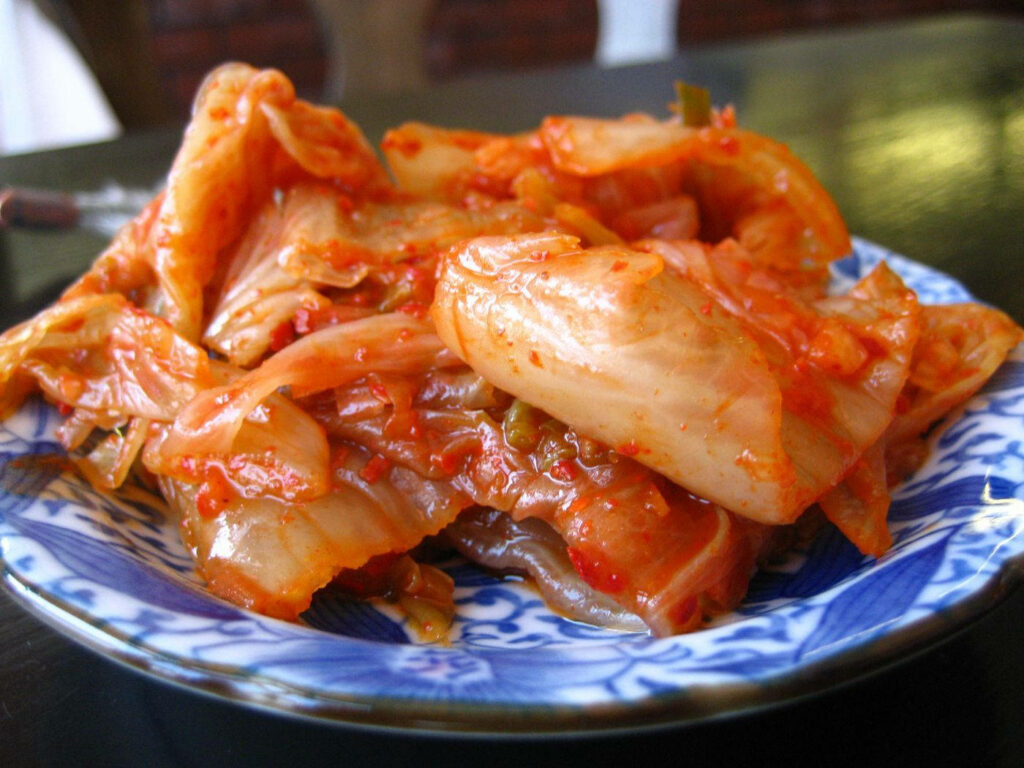 Vibrant Kimchi Closeup on Patterned Plate – Appetizing Wallpaper