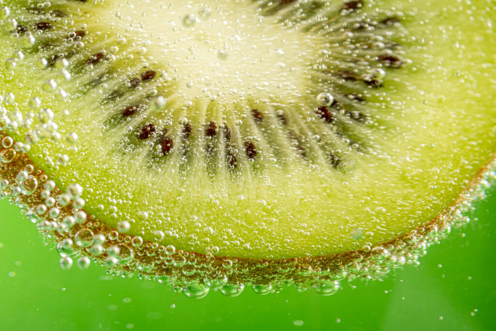 Vibrant Kiwi Slice Wallpaper with Sparkling Bubbles Background