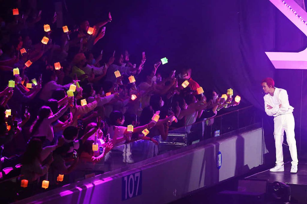 K-pop live concert with artist in white under purple lights and neon-green NCT lightsticks crowd Wallpaper