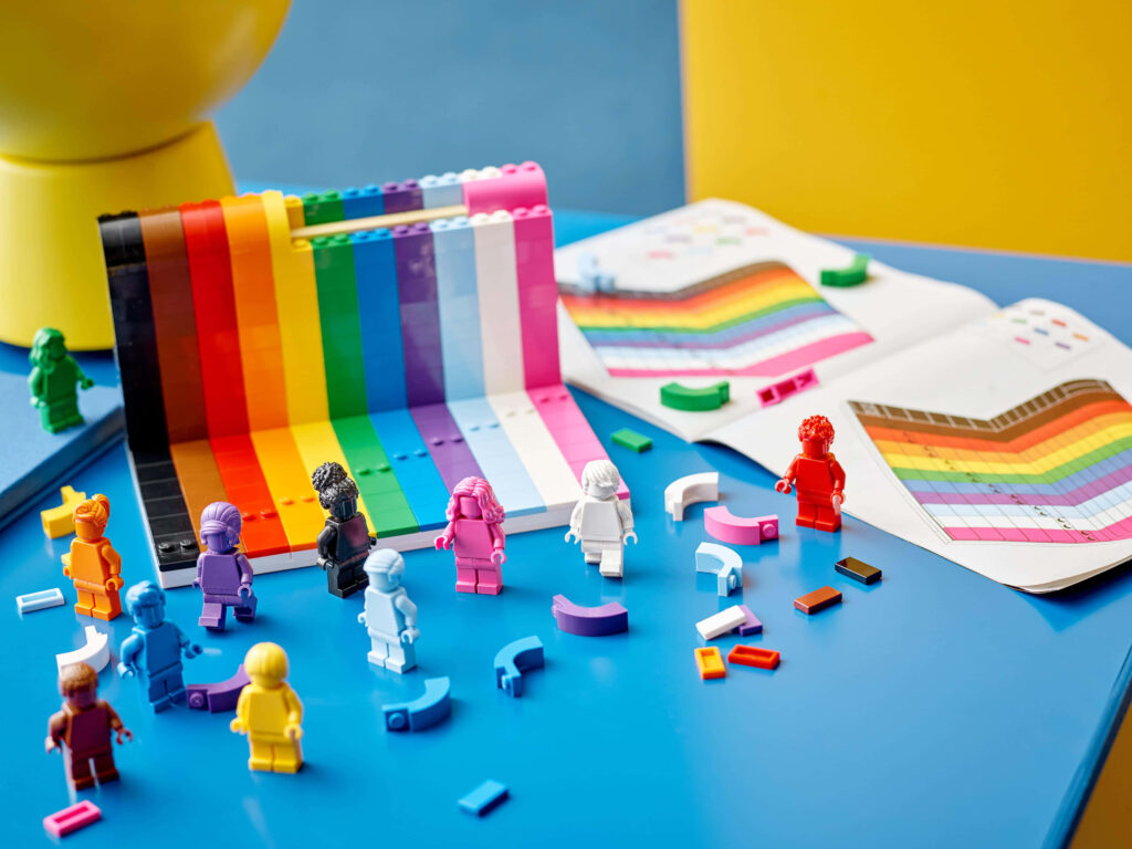 Colorful Lego minifigures around rainbow bricks with color charts on bright blue tabletop wallpaper