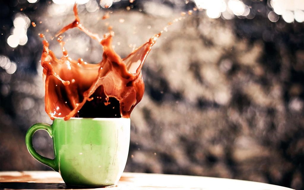 Vibrant light green mug with dynamic brown coffee splash on dark bokeh background wallpaper