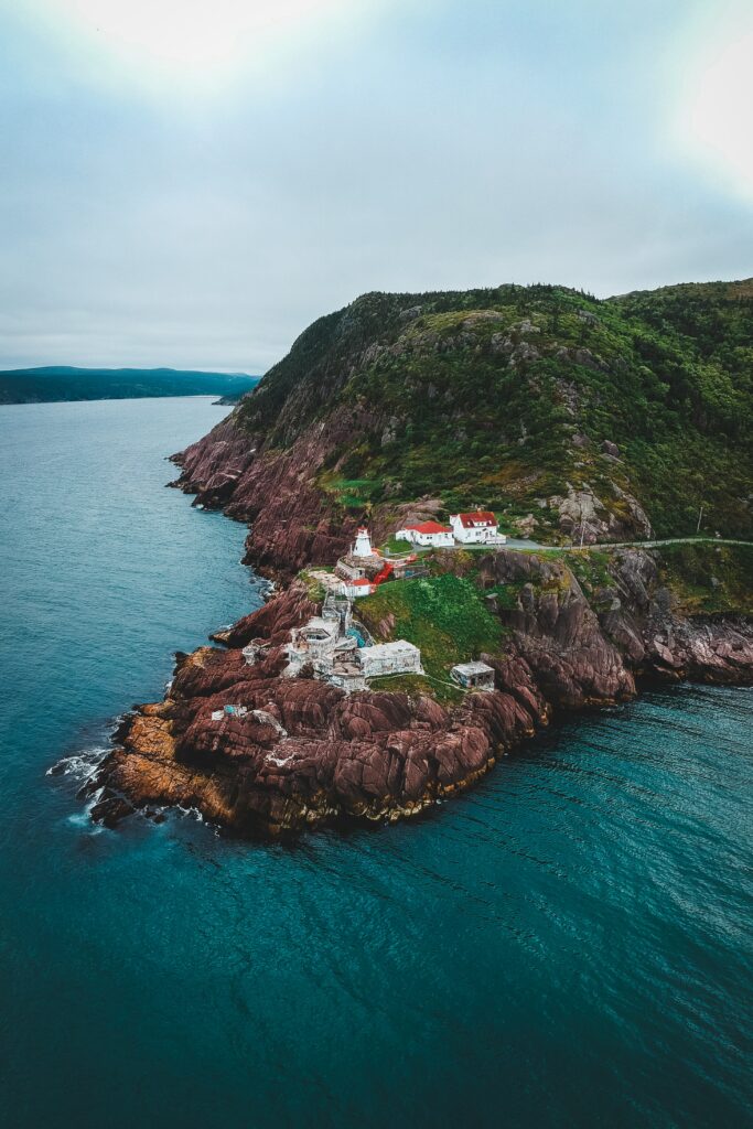 Vibrant lighthouse and coastal buildings on red cliffs overlooking deep blue sea with greenery Wallpaper