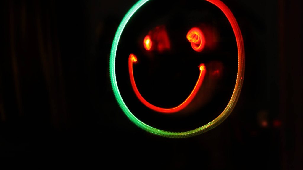 Vibrant long-exposure wallpaper glowing smiley face with green neon border and red light trails