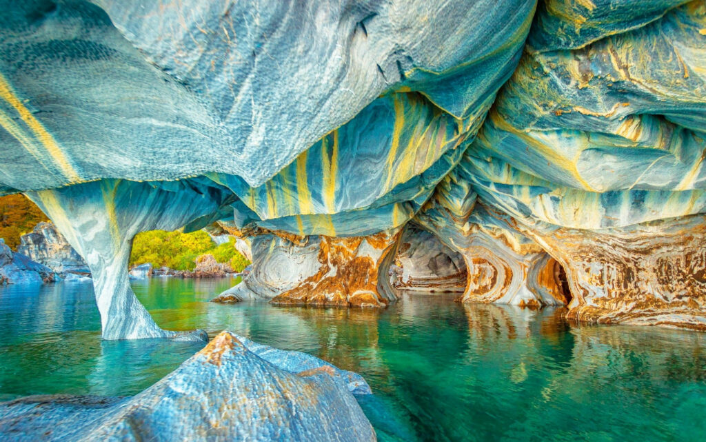 Vibrant blue and turquoise Marble Caves in Chile with sunlight on swirling rock formations Wallpaper