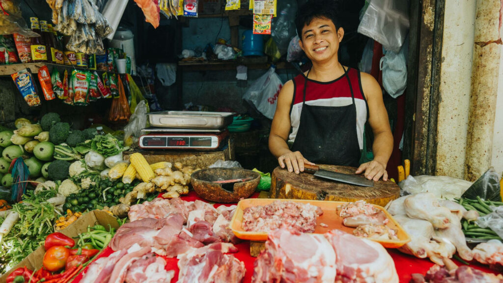 Colorful Market Stall Wallpaper: Fresh Veggies, Meats & Happy Vendor