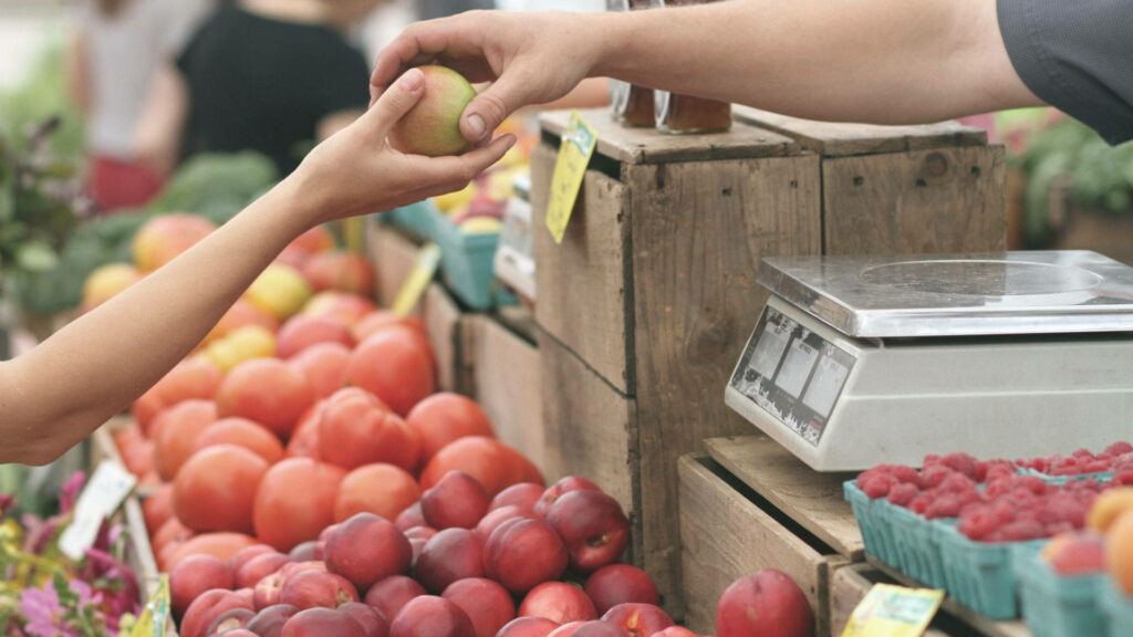 Vibrant Marketplace Scene: Hands Exchanging Fresh Fruits Wallpaper