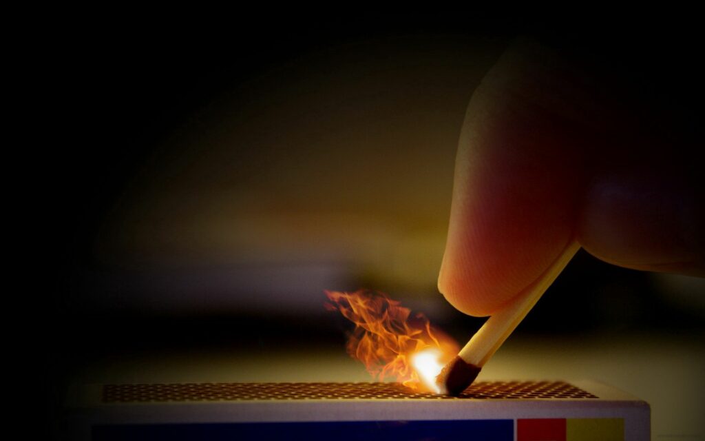Close-Up: Hand Striking Matchstick with Flame – Dark Wallpaper