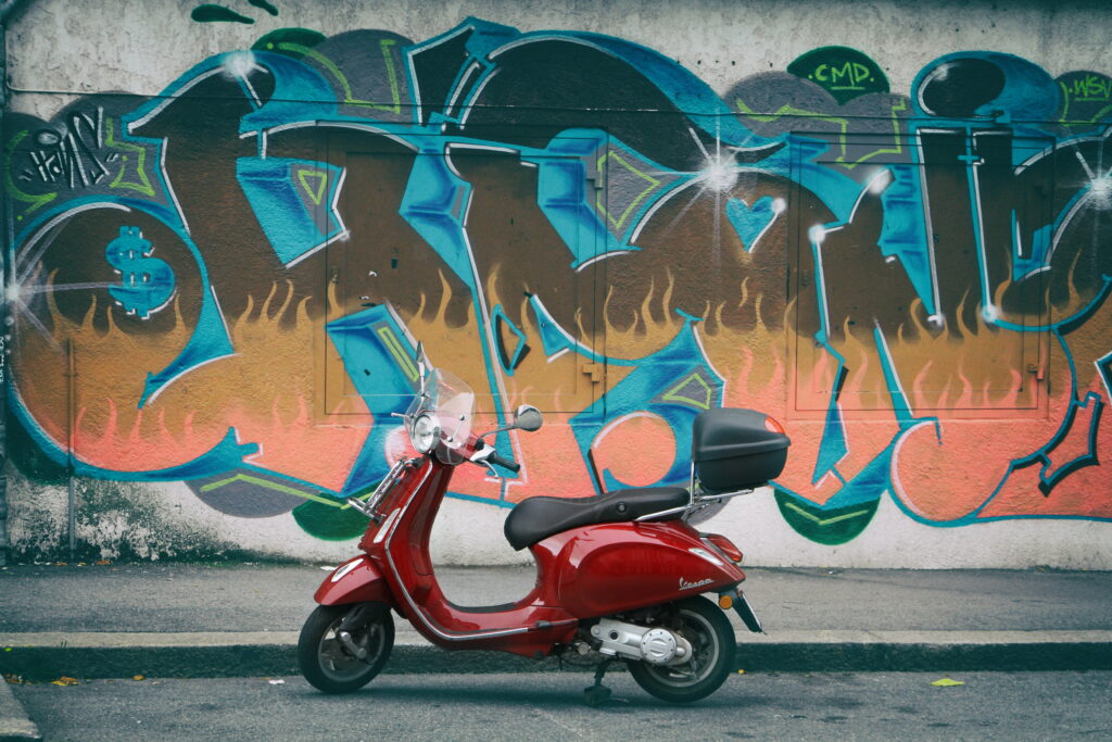 Urban Vibe: Artistic Graffiti on Red Moped Stands Against Wall as High-Definition Wallpaper Background