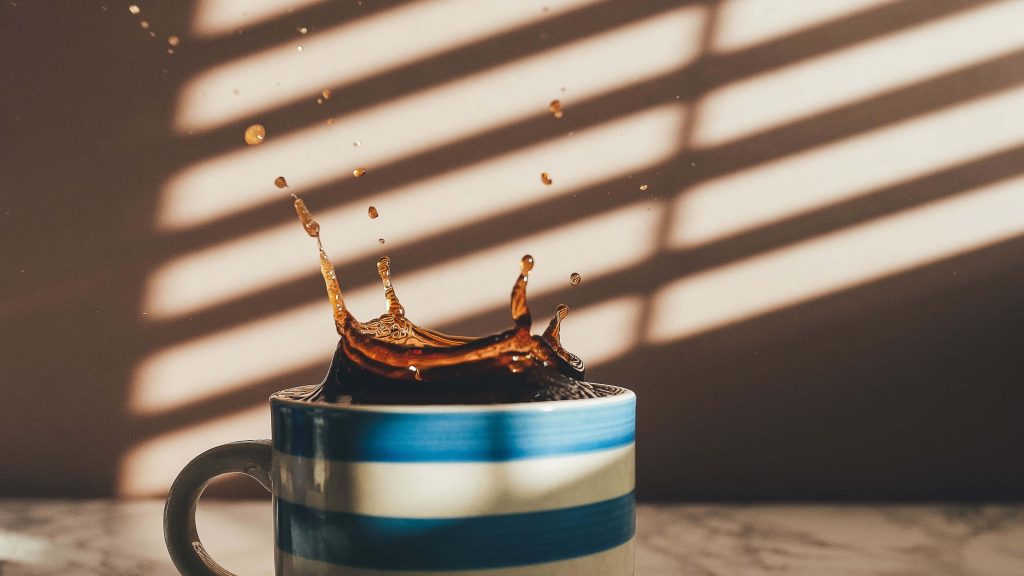 Blue and white striped mug mid coffee splash with warm sunlight and soft striped shadows background Wallpaper