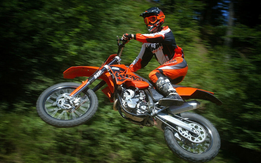 Motocross Rider Jump Wallpaper: Vivid Action in Lush Green Forest