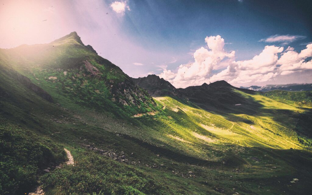 Panoramic vibrant mountain wallpaper with sunlit green slopes dramatic peaks and blue sky clouds