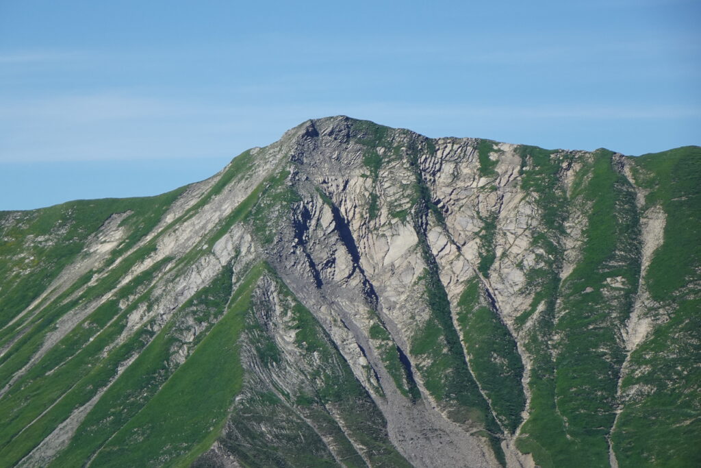 Mountain landscape wallpaper with lush green slopes rugged rocks sunlight and clear blue sky