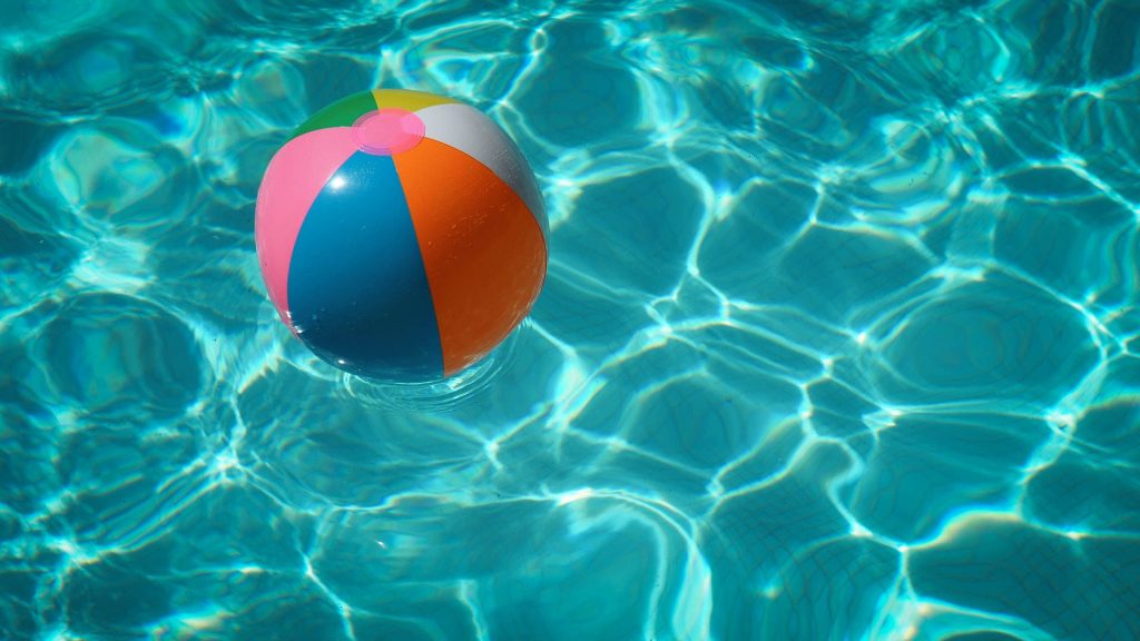 Colorful beach ball floating in clear pool water with bright sunlight and ripple reflections Wallpaper
