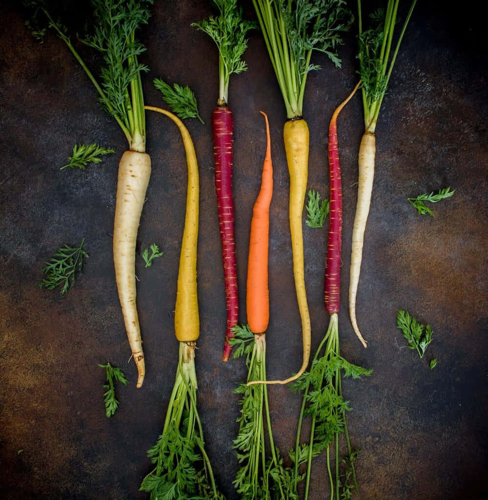 Vibrant multicolored carrots with green tops on dark textured background high contrast rustic photo Wallpaper