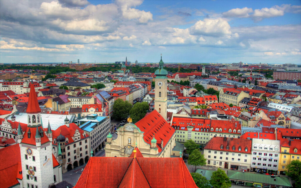 Aerial view of Munich cityscape with red roofs historic towers and modern architecture under clouds Wallpaper