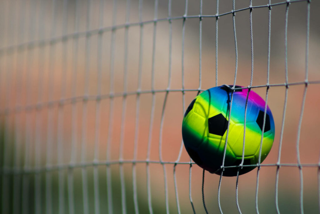 Futuristic Neon Blitz: Mesmerizing Multicolored Football Soaring Through the Gray Net Wallpaper