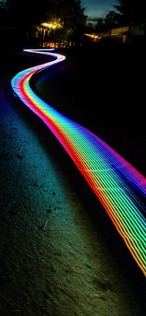 Long-exposure neon light trail in rainbow colors over dark textured night landscape wallpaper