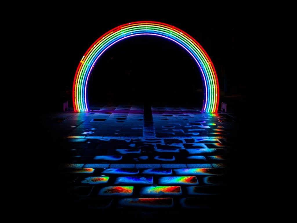 Vibrant neon rainbow arch glowing on wet pavement at night vibrant colorful wallpaper background