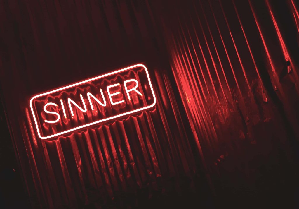 Neon red SINNER sign on dark corrugated metal creates edgy urban aesthetic wallpaper background
