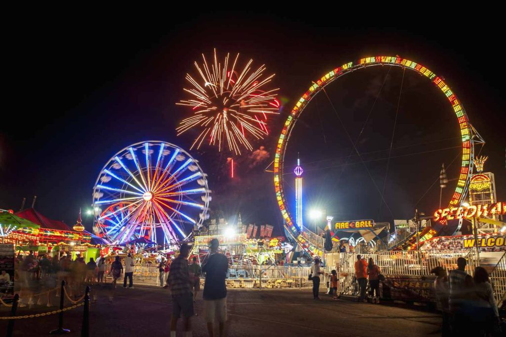 Vibrant summer night fairground with fireworks glowing Ferris wheel and thrilling carnival rides Wallpaper