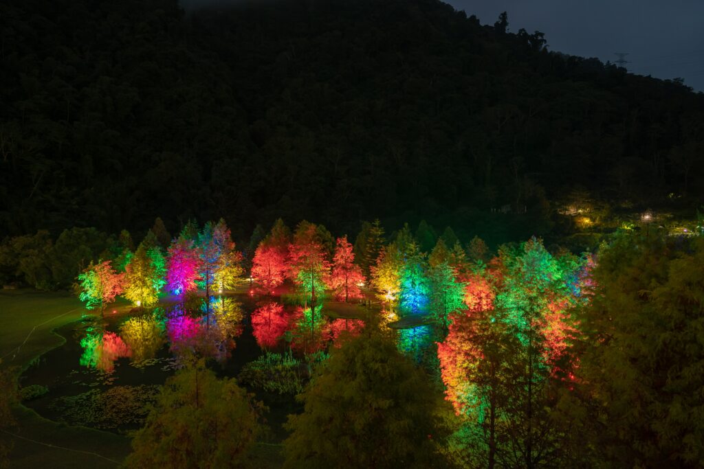 Vibrant night pond with colorful illuminated trees and vivid reflections against mountain backdrop Wallpaper