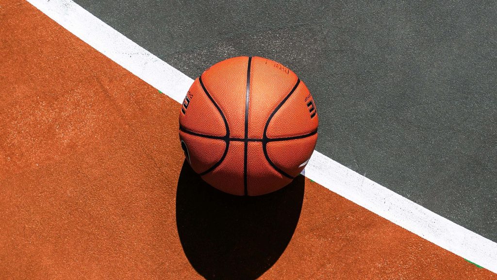 High-angle photo of vibrant orange basketball on asphalt court near white line with sharp shadow Wallpaper
