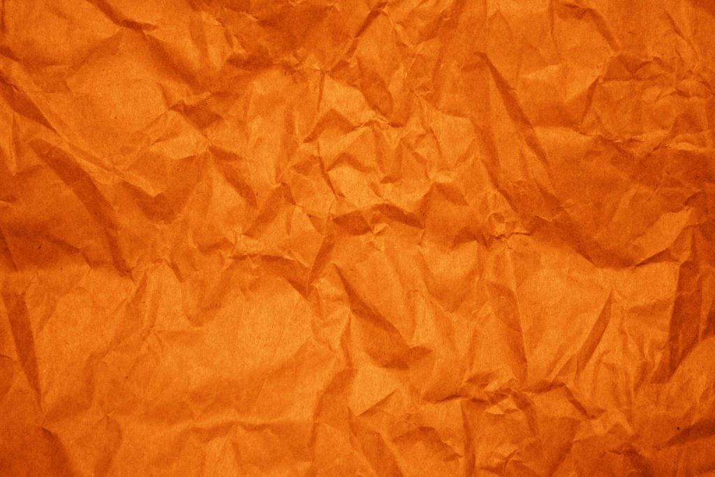 Vibrant orange crumpled paper wallpaper with deep textured folds and dynamic light shadows