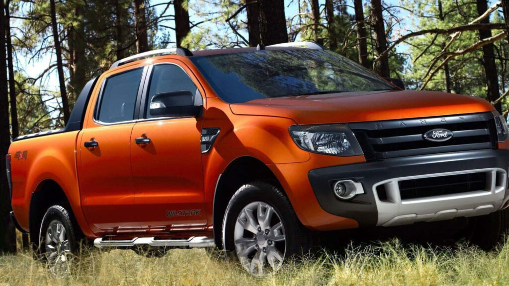 Orange Ford Ranger parked on grass with tall pine trees bold adventurous truck wallpaper