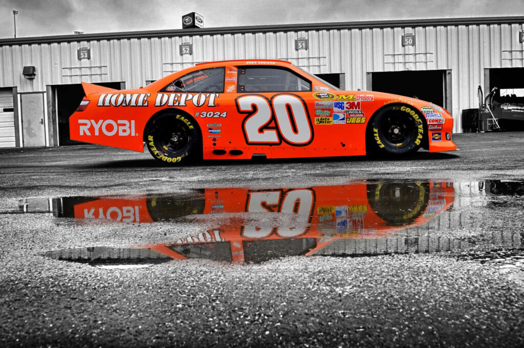 Orange NASCAR race car number 20 with Home Depot logo on wet track reflecting during championship Wallpaper