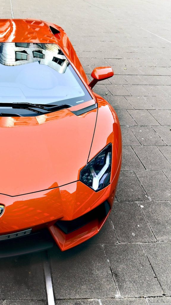 Vibrant orange Lamborghini Aventador wallpaper with Y-shaped LED headlights on textured pavement