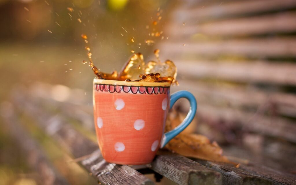 Vibrant Orange Polka-Dotted Mug with Tea on Rustic Wooden Bench Wallpaper