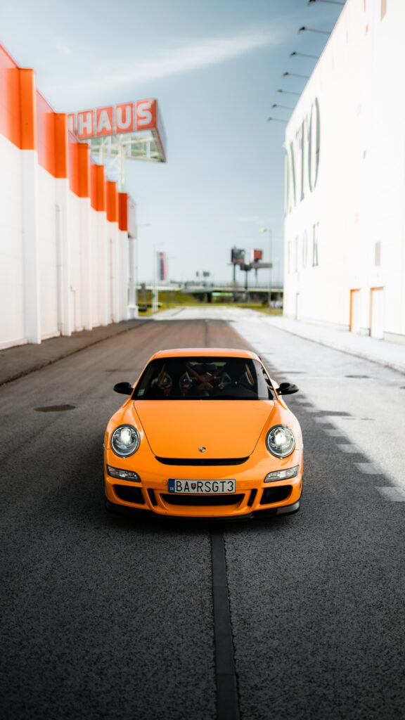 Orange Porsche 911 Wallpaper: Sleek Design on Urban Road Backdrop