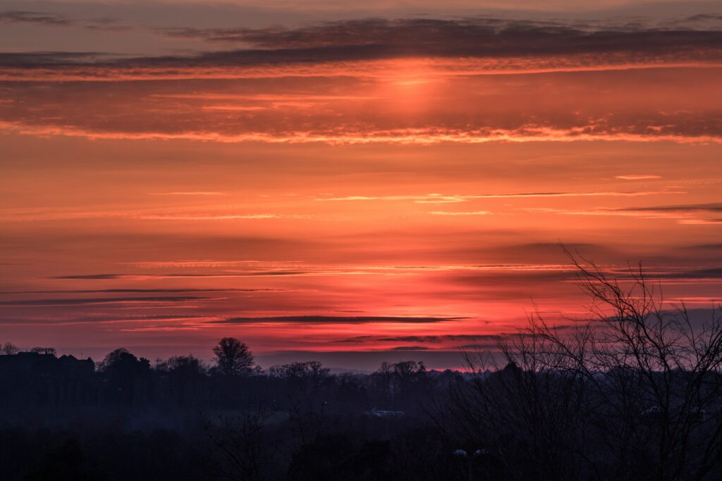 Vibrant orange red sunset with dramatic clouds and tree silhouettes peaceful wallpaper background