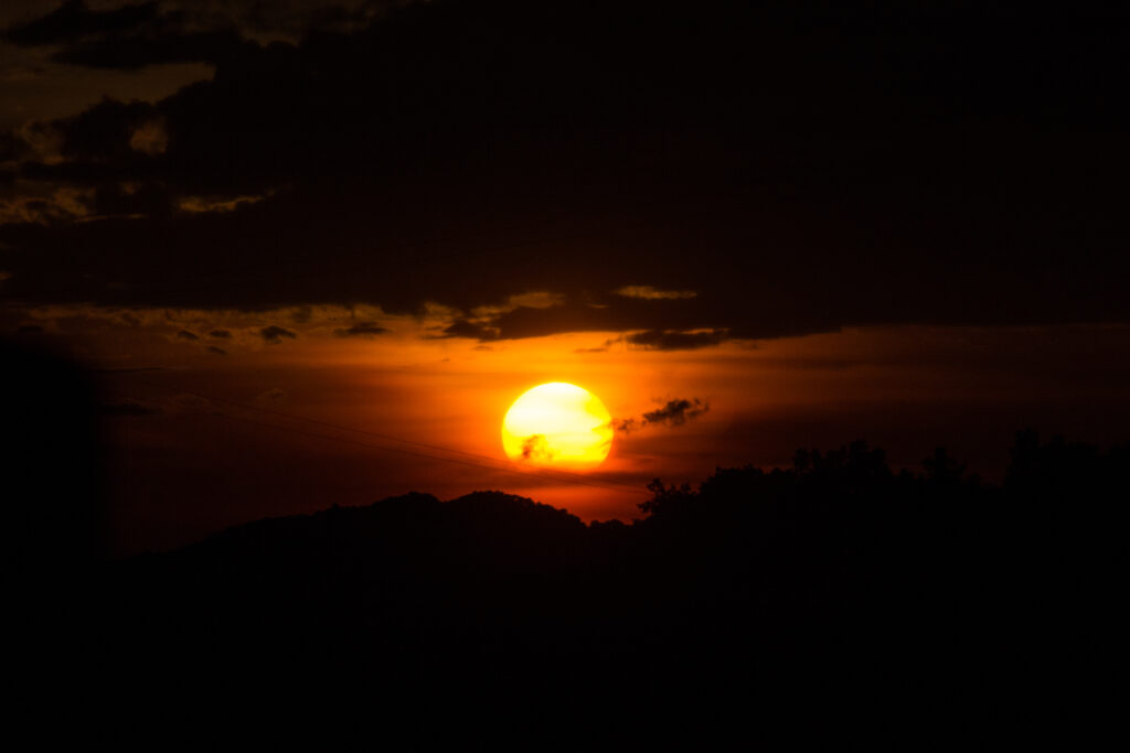 Vibrant orange sunset behind dark hills with dramatic cloudy sky serene landscape wallpaper