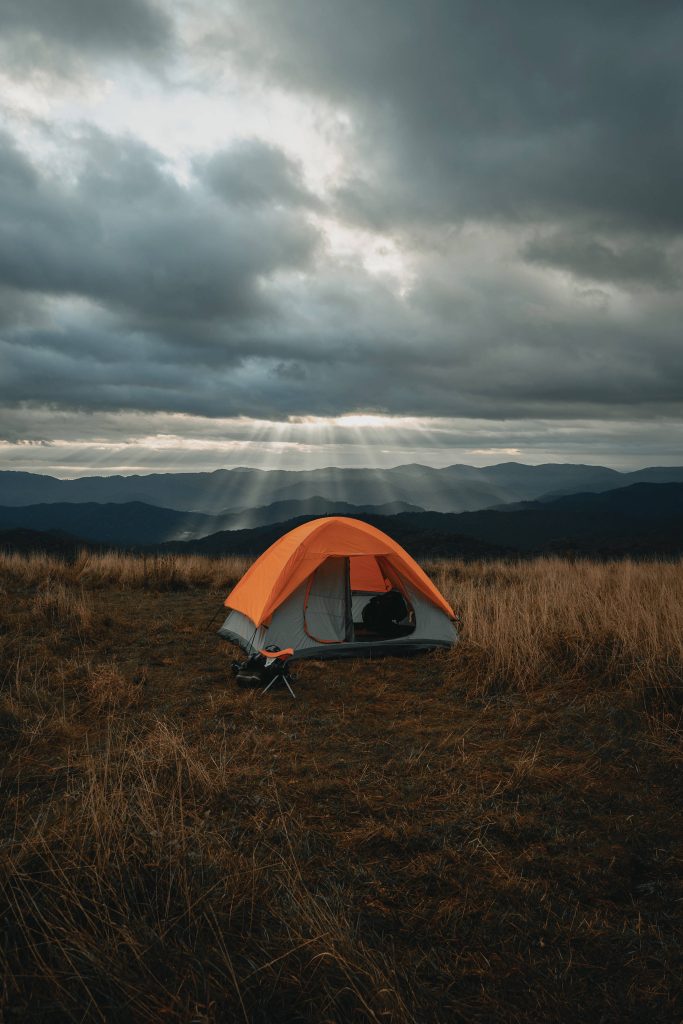 Orange tent on golden hillside with sun rays through clouds over distant mountains wallpaper