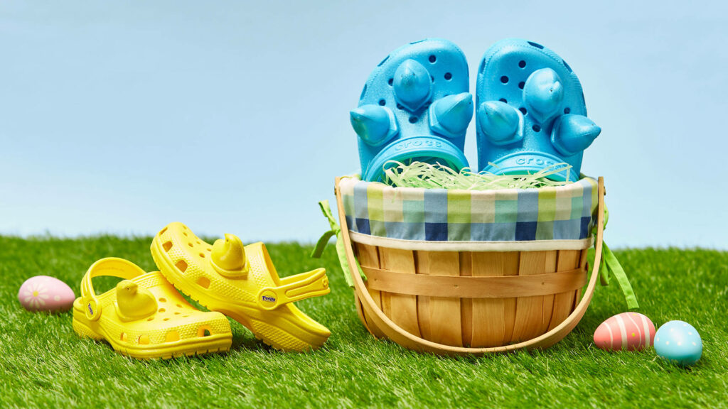 Bright blue and yellow Peeps Crocs on green grass with basket and pastel Easter eggs wallpaper